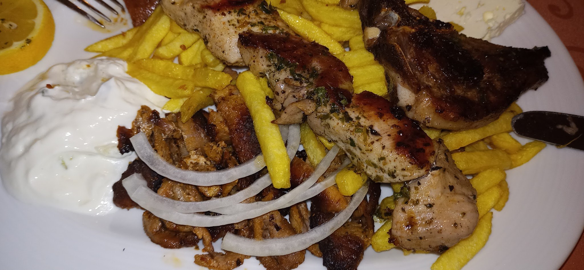 Grillteller mit Gyros, Kotelett, Pommes frites, Zwiebelringen und Zaziki