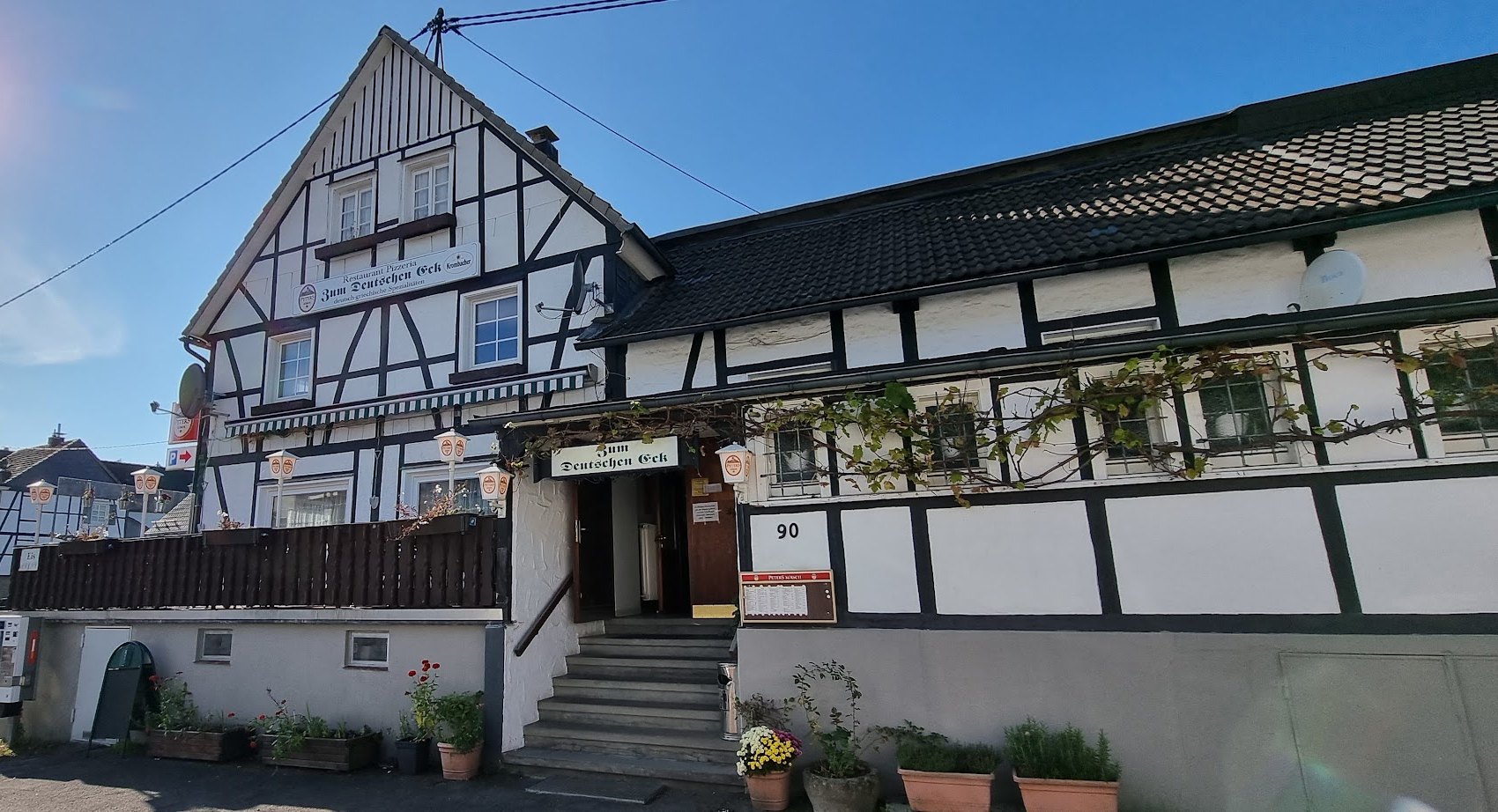 Das weiße Fachwerkhaus Zum Deutschen Eck bei Sonnenschein mit Balkon-Terrasse und Weinranken
